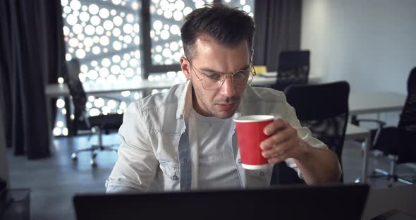 Focused Man Working on Laptop and Drinking Coffee