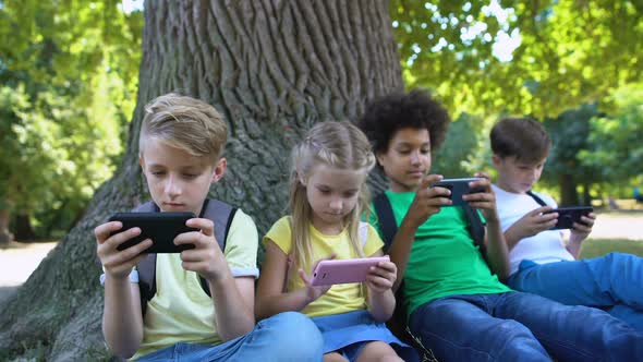 Children Playing Gadgets, Sitting Under Tree in Park, Boy Smiling in Camera, App