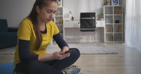 Teen Girl Is Relaxing After Training at Home Sitting on Floor and Reading Tape in Social Media alt