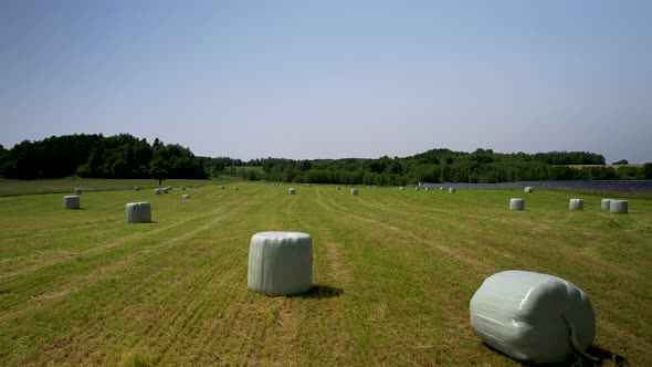 Plastic-Wrapped Hay Bales on a farm field after harvesting - aerial backward dolly alt