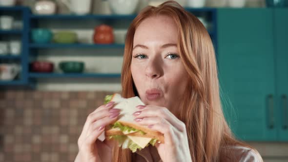 A woman in the kitchen is enjoying a sandwich alt