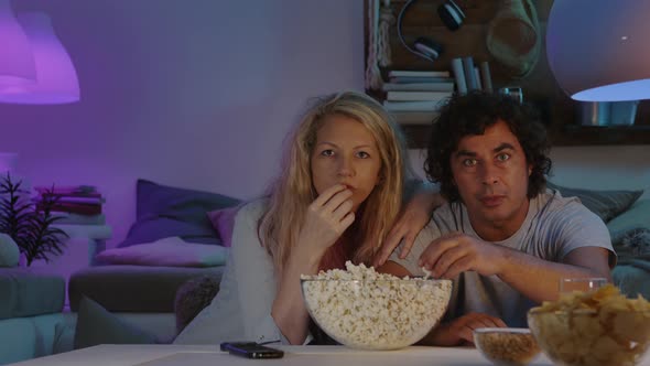 couple watching tv in the evening at home, eating popcorn