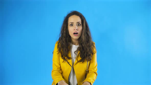 Portrait of Surprised Woman with Curly Hair Expressing Unexpectedness or Shock in Studio with Blue