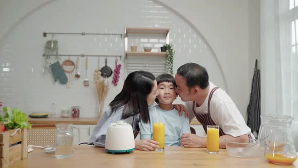 Asian family of father and mother kisses their son cooking in the kitchen.