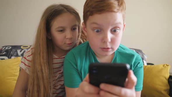 Small Children Watch Some Interesting Video on Smartphone Sitting on the Sofa at Room. Sister alt