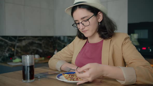 A Girl in a Hat Eating and Browsing a Mobile App alt