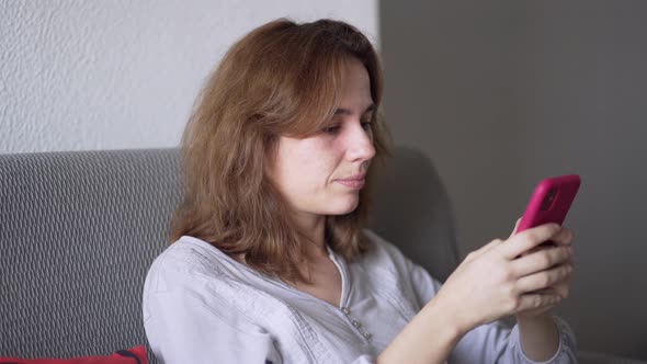 Young Woman Sitting on the Sofa in Pajamas Interacting with Mobile Phone