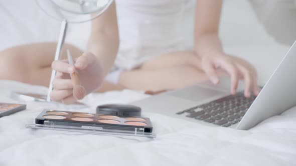 Hands of woman with learning makeup with brush on cheek on laptop computer with tutorial. alt