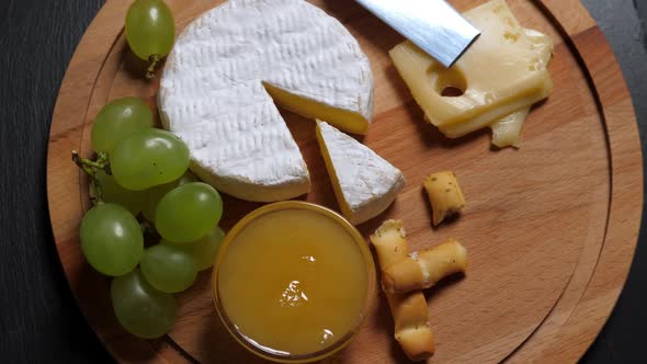 Sliced Cheese,nuts, Grape, Honey and Knife on Wooden Platter. Rotating alt