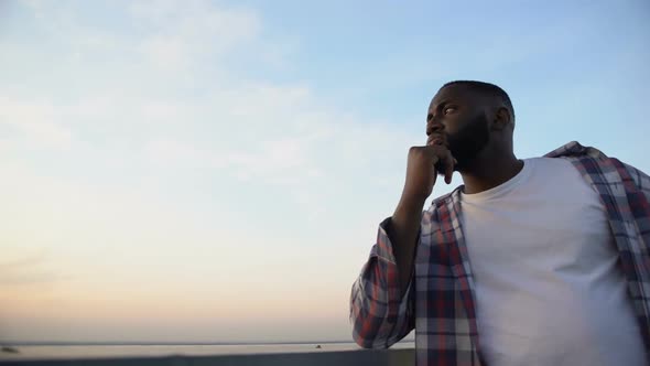 Thoughtful African-American Man Touching Chin, Watching View From Roof Top