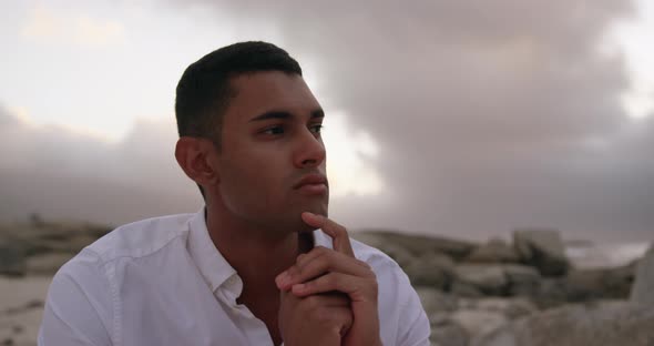 Man with hands on chin sitting on the beach 4k alt