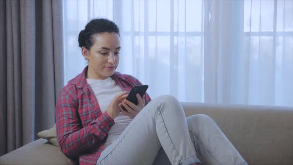 Young Serious Woman Freelancer Working on a Laptop Sitting on a Sofa at Home, Businesswoman Typing alt