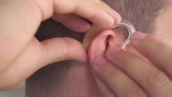 Man Inserts a Hearing Aid Into Her Ear Close Up alt