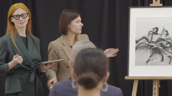 Female Auctioneer Presenting Artwork with Assistance of Female Colleague alt
