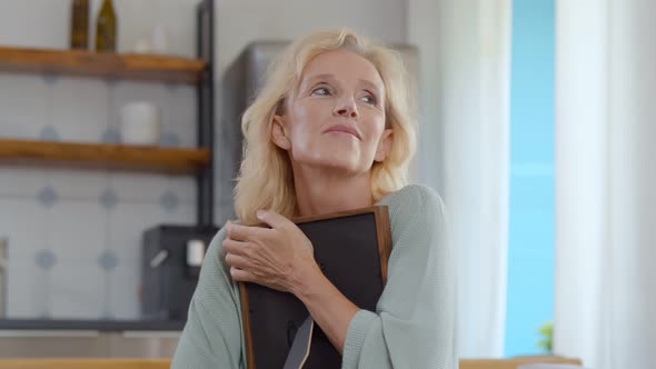 Mature Smiling Woman Looks at Old Photo in Frame at Home alt