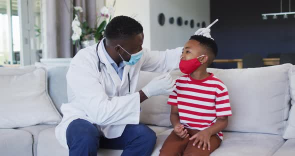 African american doctor wearing face mask taking a nasal swab sample of boy at home alt