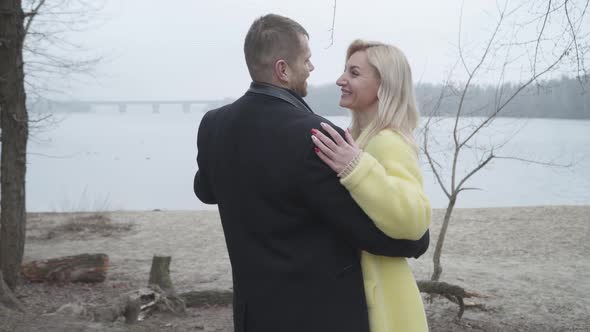 Happy Loving Caucasian Couple Hugging on Riverbank and Smiling alt