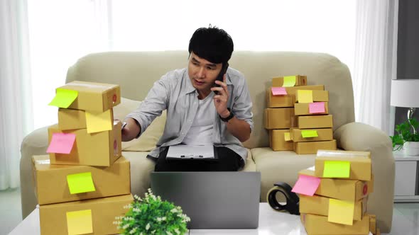 man entrepreneur talking on a mobile phone and checking parcel box of product for delivery at home