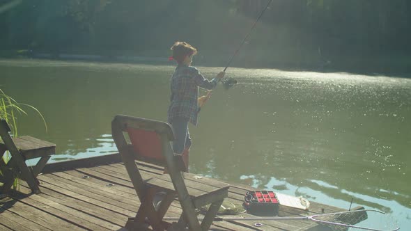 Positive Preadolescent Arab Boy with Spin Fishing Rod Fishing on Lake at Sunrise alt