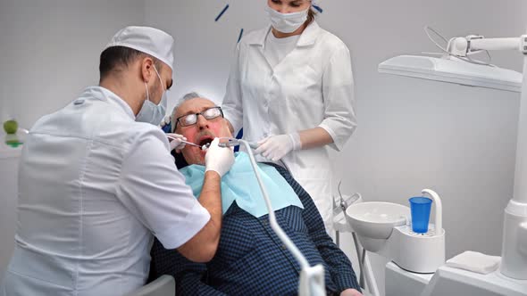 Male Stomatologist Working with Aged Patient Treating Teeth Using Equipment alt