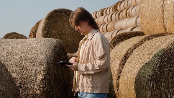 Farmer Agronomist Checks Hay Bales on the Wheat Field After Harvest at Sunset alt