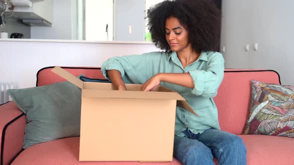 Cheerful Happy Multiracial Woman Unpack Cardboard Box Shipping Sitting on the Sofa at Home