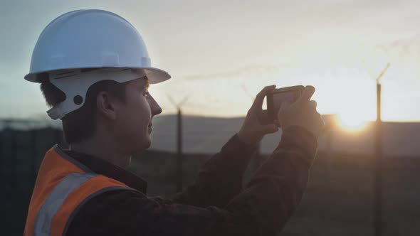 A Male Engineer Takes a Photo of a Plantation or Solar Panel Plant on a Smartphone alt