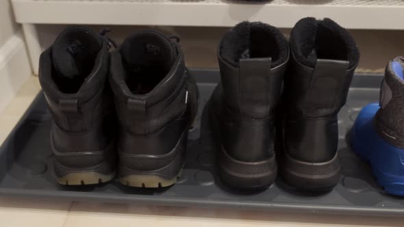 Family Winter Boots Lined Up on Hallway Rug Men Women and Tiny Baby Shoes alt