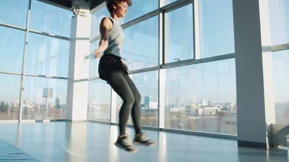 Young Woman in Sportswear Jumping with Skipping Rope Indoors in Modern Gym alt