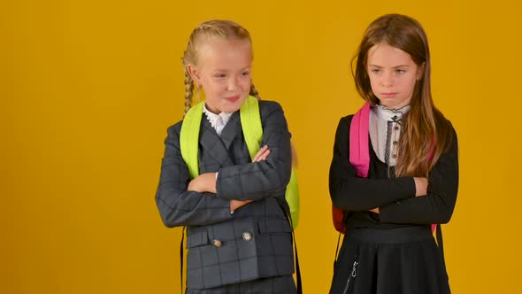 Two little schoolgirls in school uniforms with backpacks are not friendly