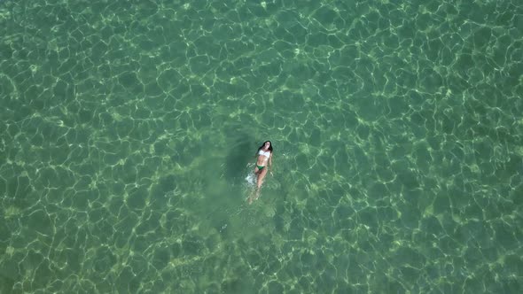 Woman in a bikini swims and splashes in the green, shimmering waters of the Aegean Sea; Paros island alt
