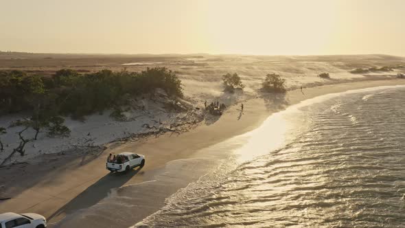 Kite surfers on pickup trucks arriving at Guriu beach in warm sunset glow; drone alt
