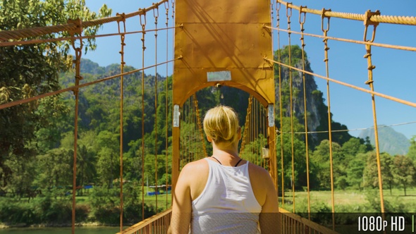 Woman Walking on Wood Suspension Bridge Walkway in the Mountains of Vang Vieng, Laos alt