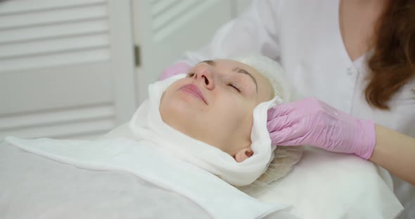 A Gloved Cosmetologist Cleans The Skin With A Napkin In A Cosmetology Clinic. alt