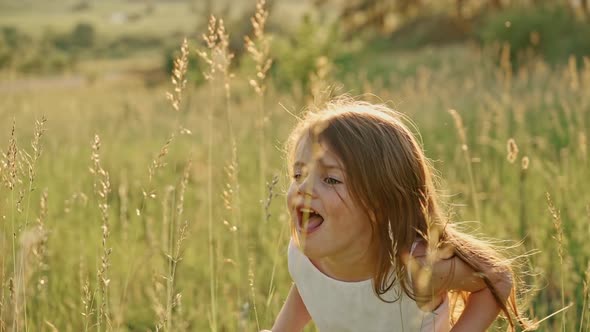 Portrait of a Cute Girl with Flowing Hair in a White Summer Dress Standing on a Green Lawn Smiling alt