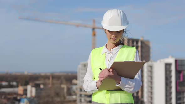 Portrait of Young Woman Engineer Who is Making Entries in Documents alt