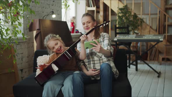 Woman and Her Daughter Playing the Guitar and Fooling Around alt