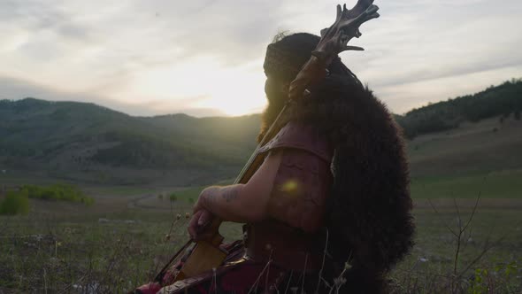 Calm Man in Shaman Clothes Sits Leaning on Ikili in Valley alt