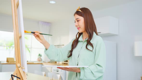 Asian young talented woman artist coloring on painting board in house. alt