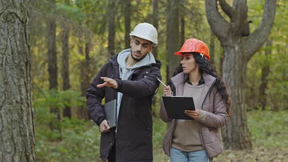 Young Diverse Employees in Helmets Indian Man and Oriental Woman Forestry Engineers in Hardhats with alt