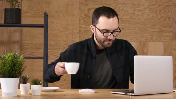 Young Bearded Man Drinking Coffee or Tea While Working on Laptop alt