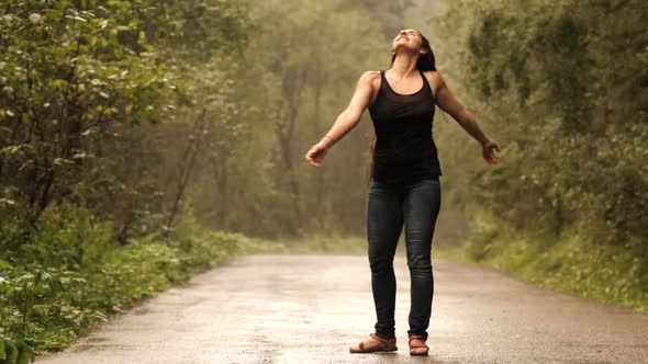 Slow Motion of a Young Happy Woman Dancing in the Summer Rain on a Road in the Forest.