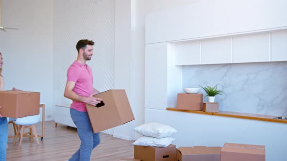 Joyful couple puts large cardboard boxes on stack on new flat floor alt