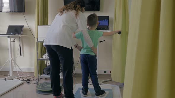 Rehabilitation Centre Evexia, female doctor examines small boy by special equipment in clinic room alt