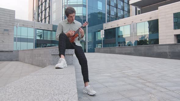 Young Adult Man Performs with Exotic Musical Instrument in Downtown on Modern Glass Office Building alt