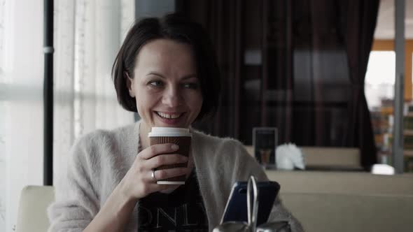 Beautiful Brunette Drinks Coffee From a Cup and Laughs