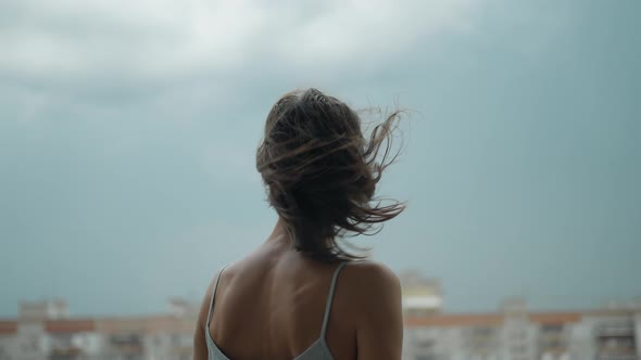 Rear View of a Young Woman Standing on Balcony at Home in Nightware Dramatic Sky on Background alt