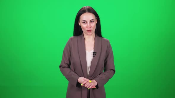 Female Reporter in Suit Looks Into the Camera and Speaks Into a Lavalier Microphone on a Green alt