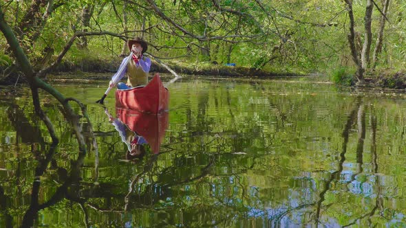 Cowboy in a Canoe Floats on the River in the Forest alt
