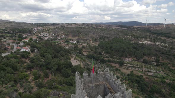 Drone aerial backward view of Sortelha medieval castle and wind turbines in background, Portugal